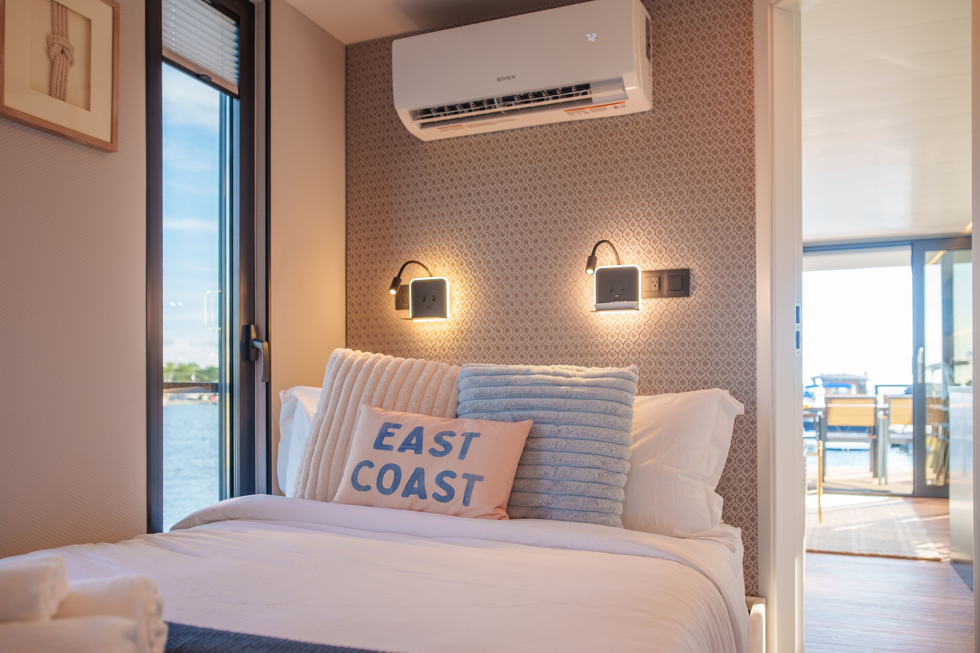 A hotel room with a bed, a window, an air conditioning unit, and a view of the sea.
