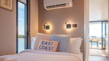 A hotel room with a bed, a window, an air conditioning unit, and a view of the sea.