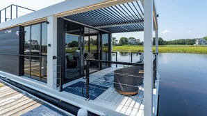A modern, glass-enclosed boat with a deck area featuring a seating arrangement and a covered section.