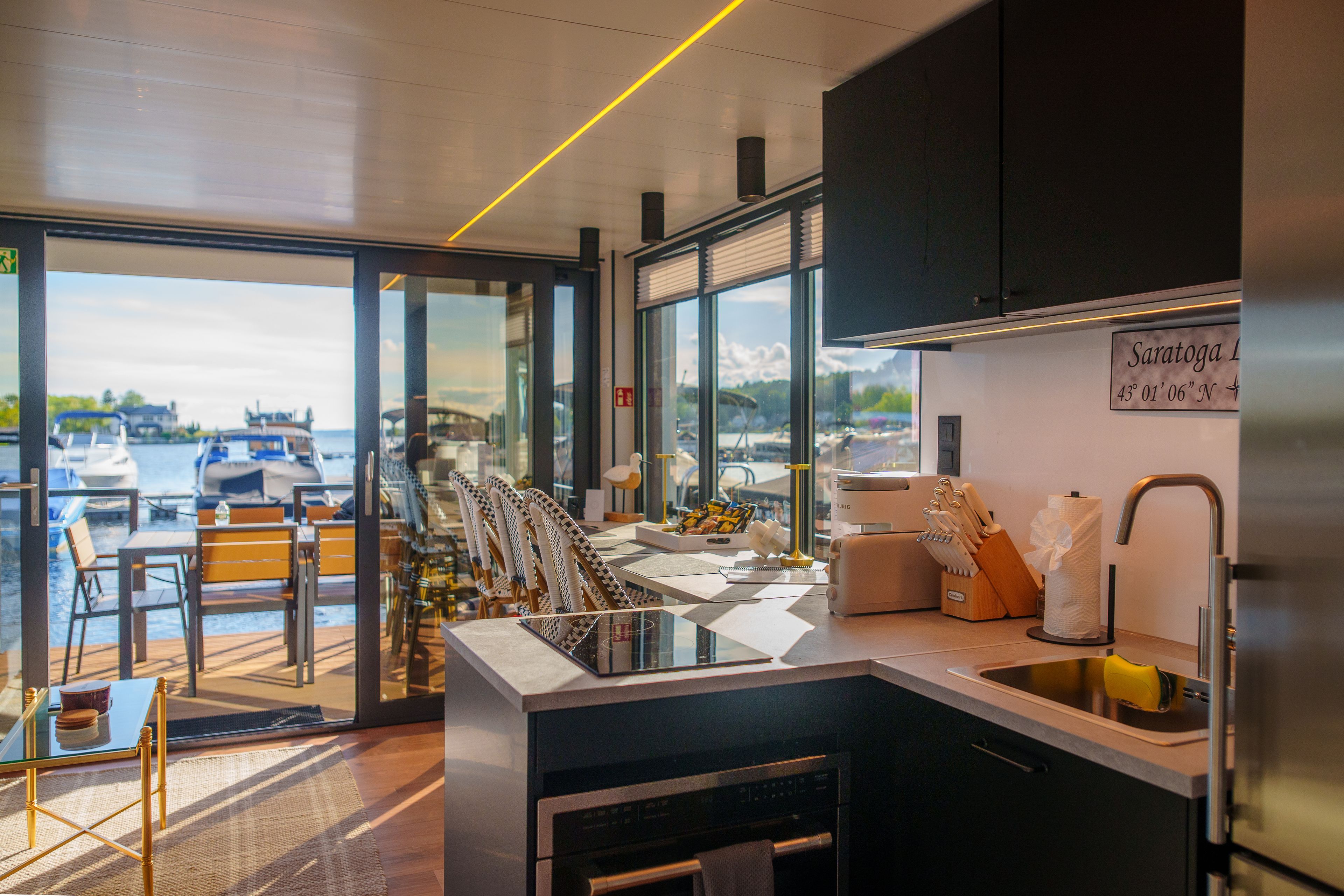 Une cuisine moderne avec vue sur un port de plaisance, équipée d’un évier, d’une cuisinière et de divers appareils de cuisine.