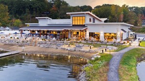A modern building with a covered patio area, outdoor seating, and a small pond.