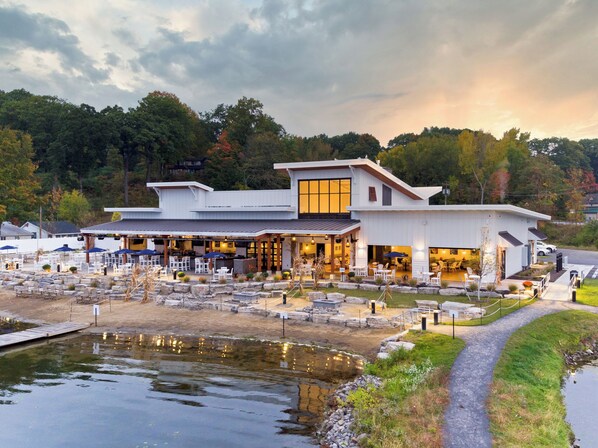 A modern building with a covered patio area, outdoor seating, and a small pond.