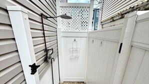 Un étroit sentier extérieur mène à une porte blanche, bordée de clôtures blanches et d’une structure en treillis.