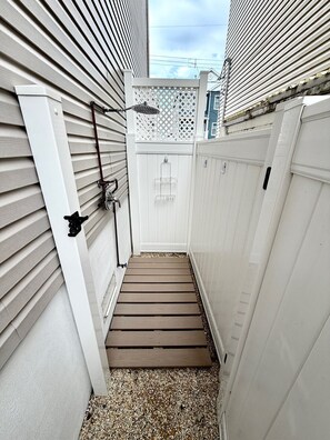 A narrow outdoor pathway leading to a white door, flanked by white fences and a lattice structure. - Luxury Bayside Ortley Beach House • Sleeps 10 (Seaside Heights)