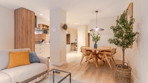 Un salon moderne comprenant un canapé, une table basse, une table à manger et des chaises. On aperçoit une cuisine à l’arrière-plan, avec des placards et un four à micro-ondes.