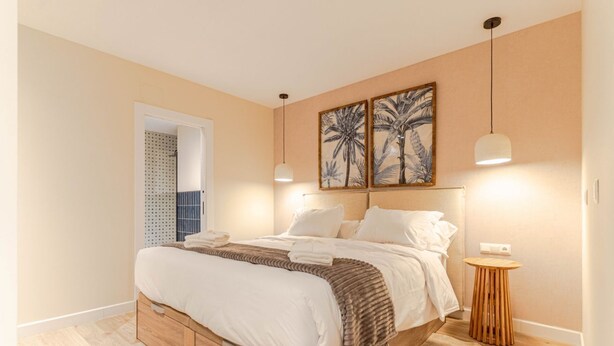 Une chambre avec un lit, un plancher en bois, une petite table d’appoint ronde en bois et deux lampes suspendues fixées au mur.