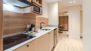 Une cuisine moderne équipée d’un four à micro-ondes, d’une cuisinière et d’un évier encastrés. Une étagère en bois se trouve au-dessus du four à micro-ondes, et une petite plante y est posée.