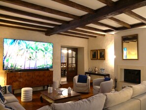 A living room with a television, sofas, a fireplace, and wooden beams on the ceiling. - Beautiful Charente residence - heated swimming pool (Saint-Palais-du-Né)