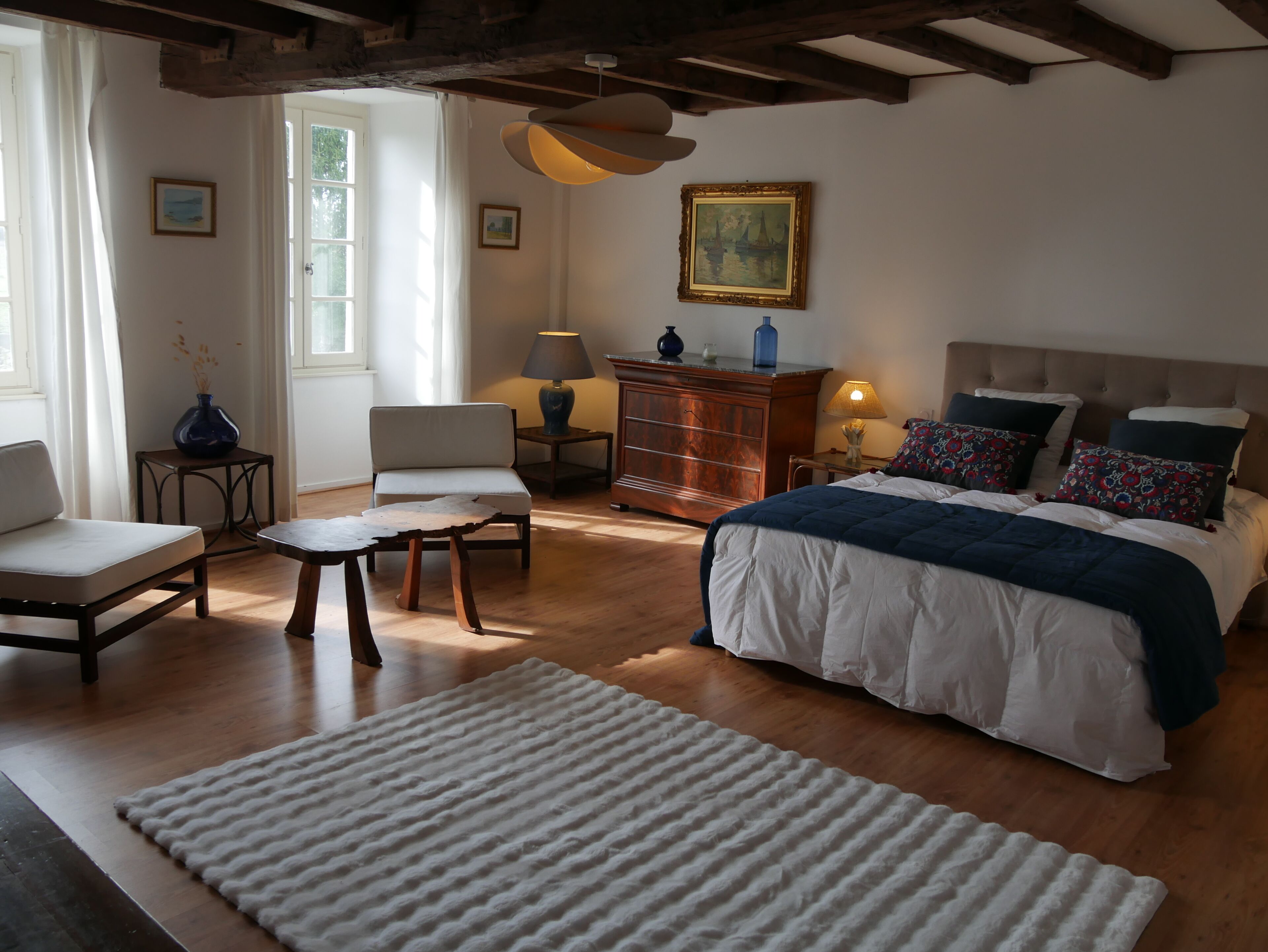 A bedroom with a bed, a chair, a small table, a dresser, and a window.