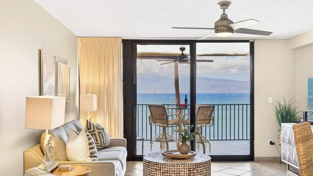 Un balcon équipé d’un ensemble de mobilier de jardin et d’un canapé, d’un ventilateur de plafond et offrant une vue sur l’océan.