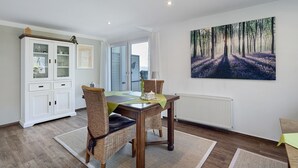 Un coin repas comprenant une table, des chaises, un buffet et un grand tableau représentant une forêt, accroché au mur.