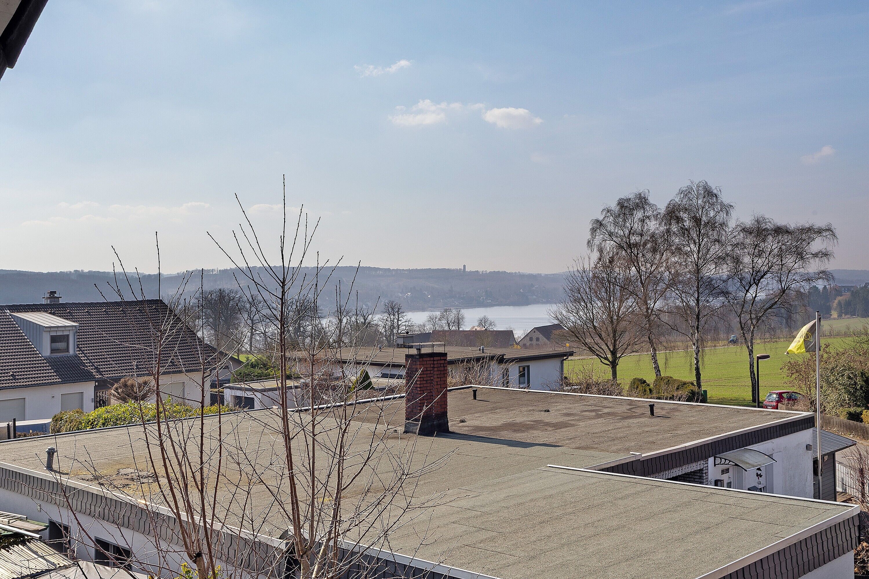 A residential building with a flat roof, a chimney, and a view of a lake and distant trees.