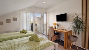 Une chambre d’hôtel avec deux lits, un bureau, une chaise, une télévision et une plante en pot.
