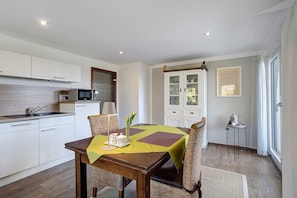 Une cuisine moderne avec des meubles blancs, un four à micro-ondes et un coin repas avec une table dressée pour deux personnes.