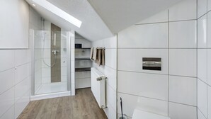 Casa de banho moderna com cabine de duche em vidro, porta-toalhas embutido e sanita com bidé fixo na parede.