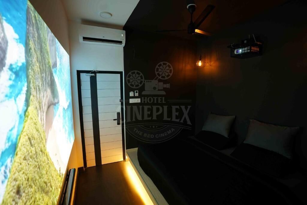 A hotel room with a large screen displaying a nature scene, a bed, and a wall with the hotel's logo.