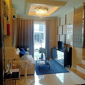 Un salón moderno con candelabro, sofá con cojines, ventilador, mesa de centro y televisor sobre un mueble.
