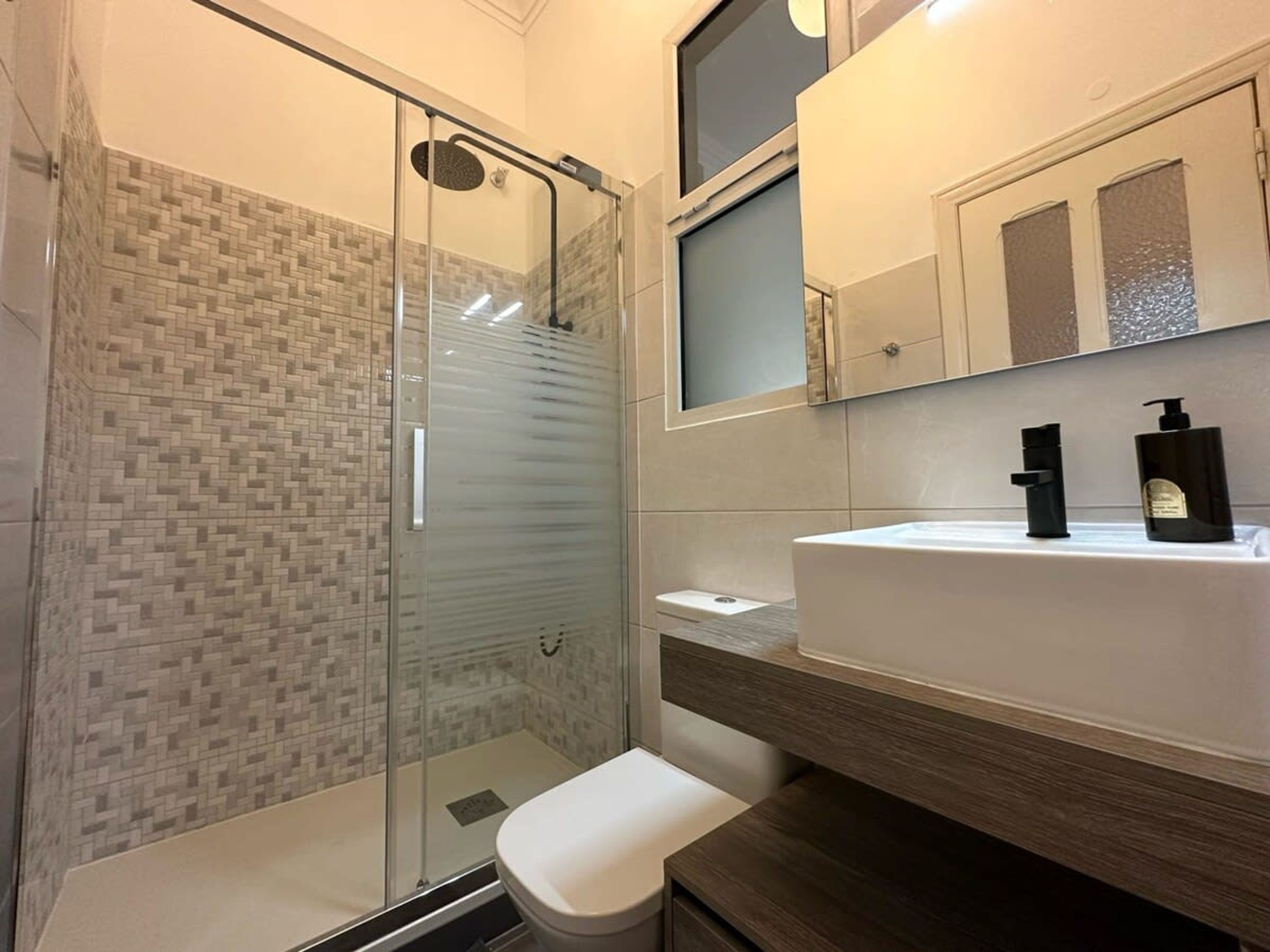 A modern bathroom with a glass shower enclosure, a white sink, and a wooden vanity.