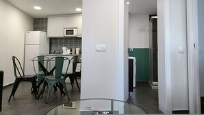 Una cucina moderna con mobili bianchi, un forno a microonde e una macchina per il caffè. C'è un'area pranzo con un tavolo in vetro e sedie.