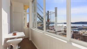 Un balcon donnant sur un port et sur des bâtiments, une table blanche et une chaise blanche.