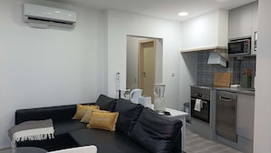 Una sala de estar moderna con un sofá de cuero negro, una mesa de centro de vidrio y un área de cocina con microondas, lavavajillas y licuadora.