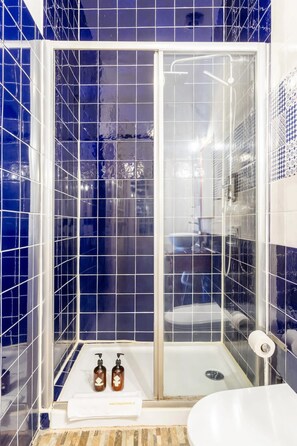 A bathroom with blue-tiled walls, a glass-enclosed shower, and a white sink. - Artistic Alfama 4BR Cathedral Views Tram 28 (Lisbon)