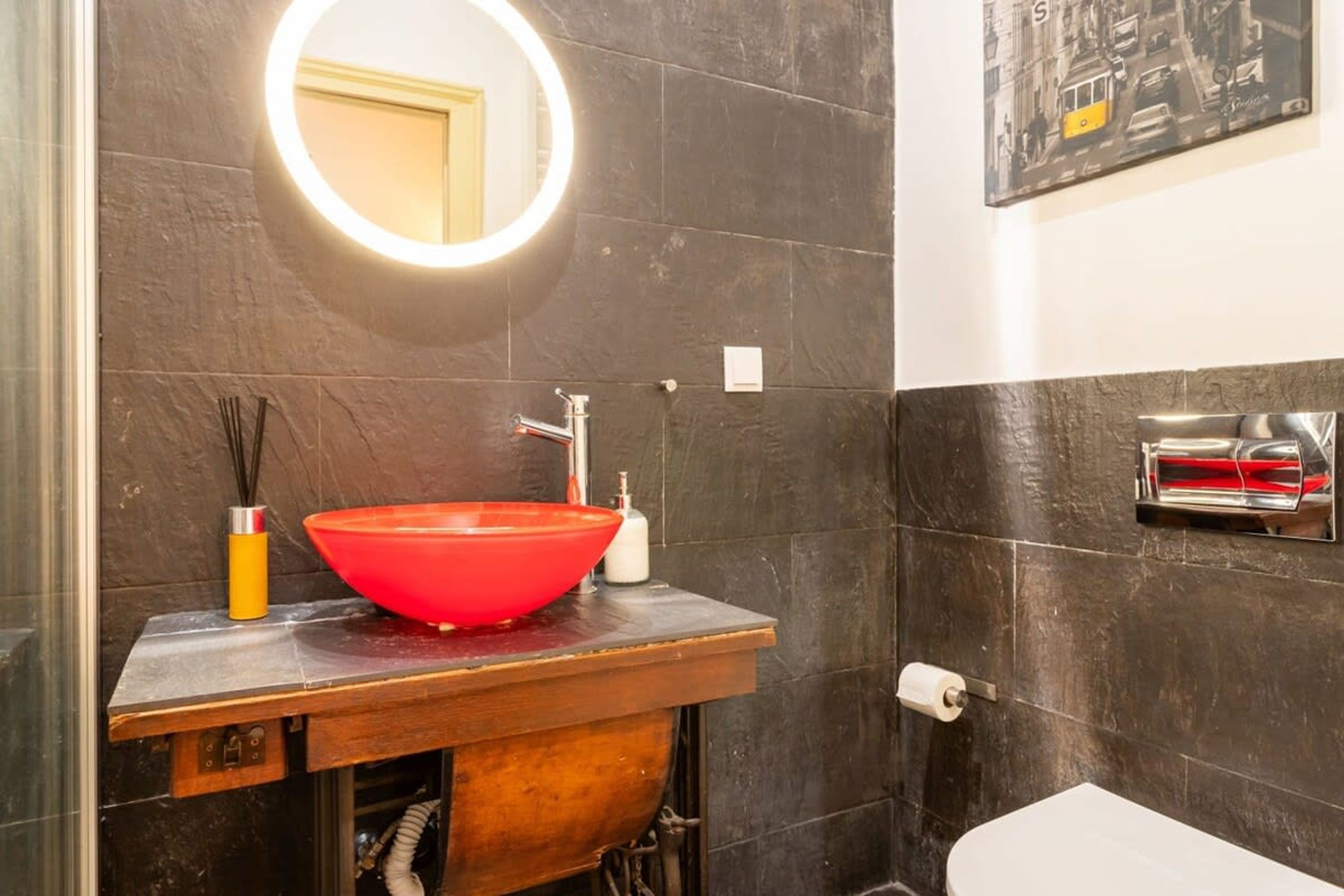 Un baño con un espejo redondo, un lavabo rojo, un toallero y un inodoro.