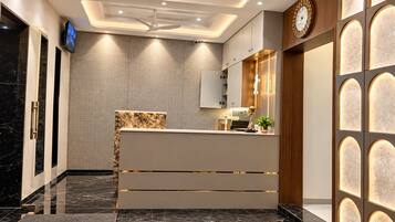 Un área de recepción moderna con piso de mármol, un mostrador de recepción, un reloj en la pared y un ventilador de techo.