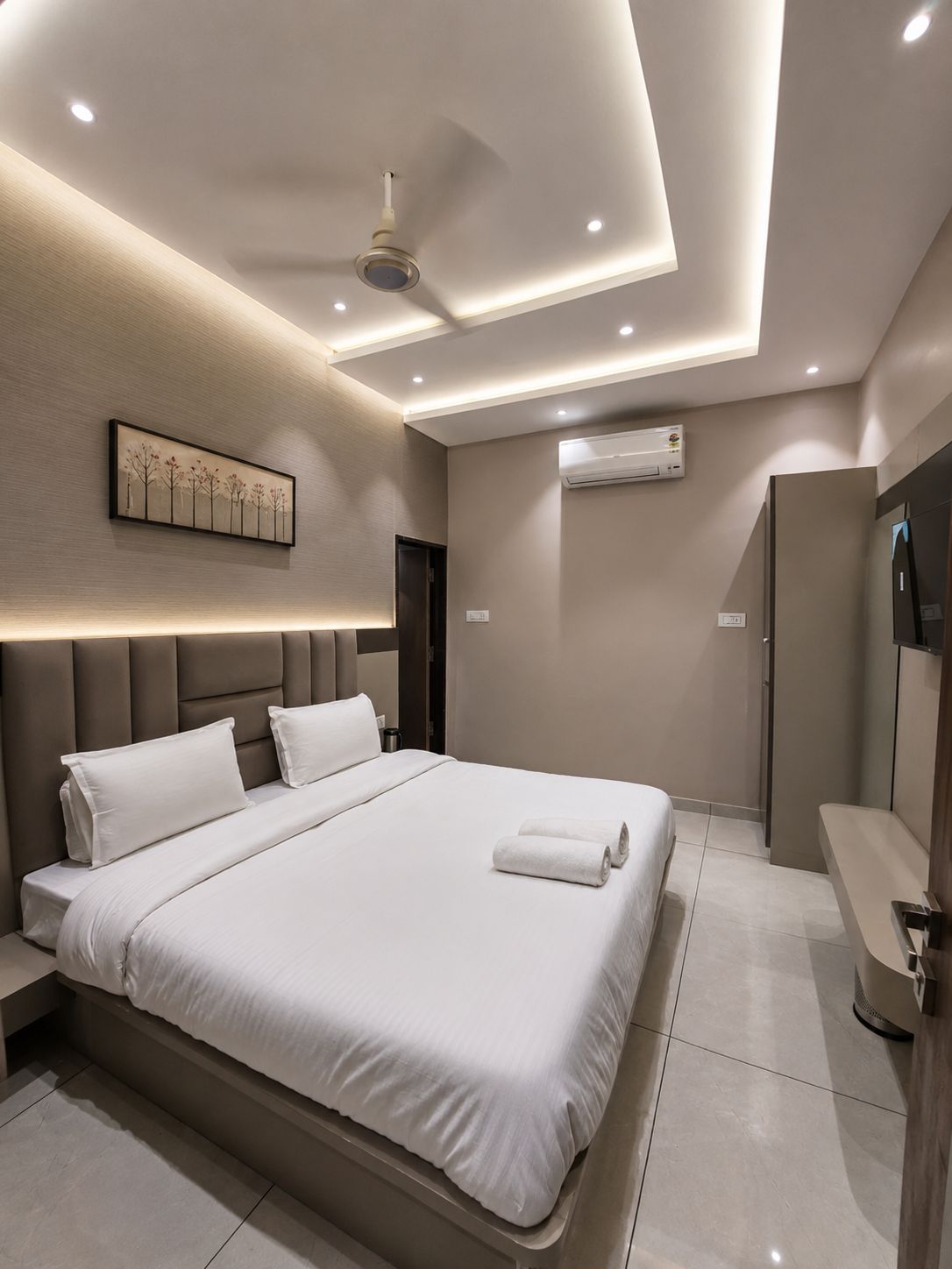 Un dormitorio moderno con una cama grande, ventilador de techo, luces empotradas, equipo de aire acondicionado y una obra de arte enmarcada en la pared.
