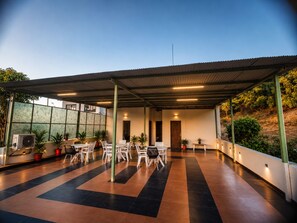 An outdoor covered patio area with multiple tables and chairs, potted plants, and a large air conditioning unit. - HOTEL GEETANJALI (Mount Abu)