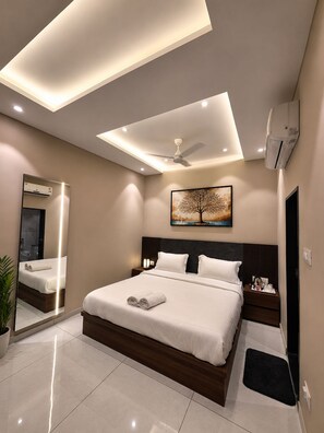 A modern hotel room with a large bed, a ceiling fan, recessed lighting, a painting, and a mirror. - HOTEL GEETANJALI (Mount Abu)