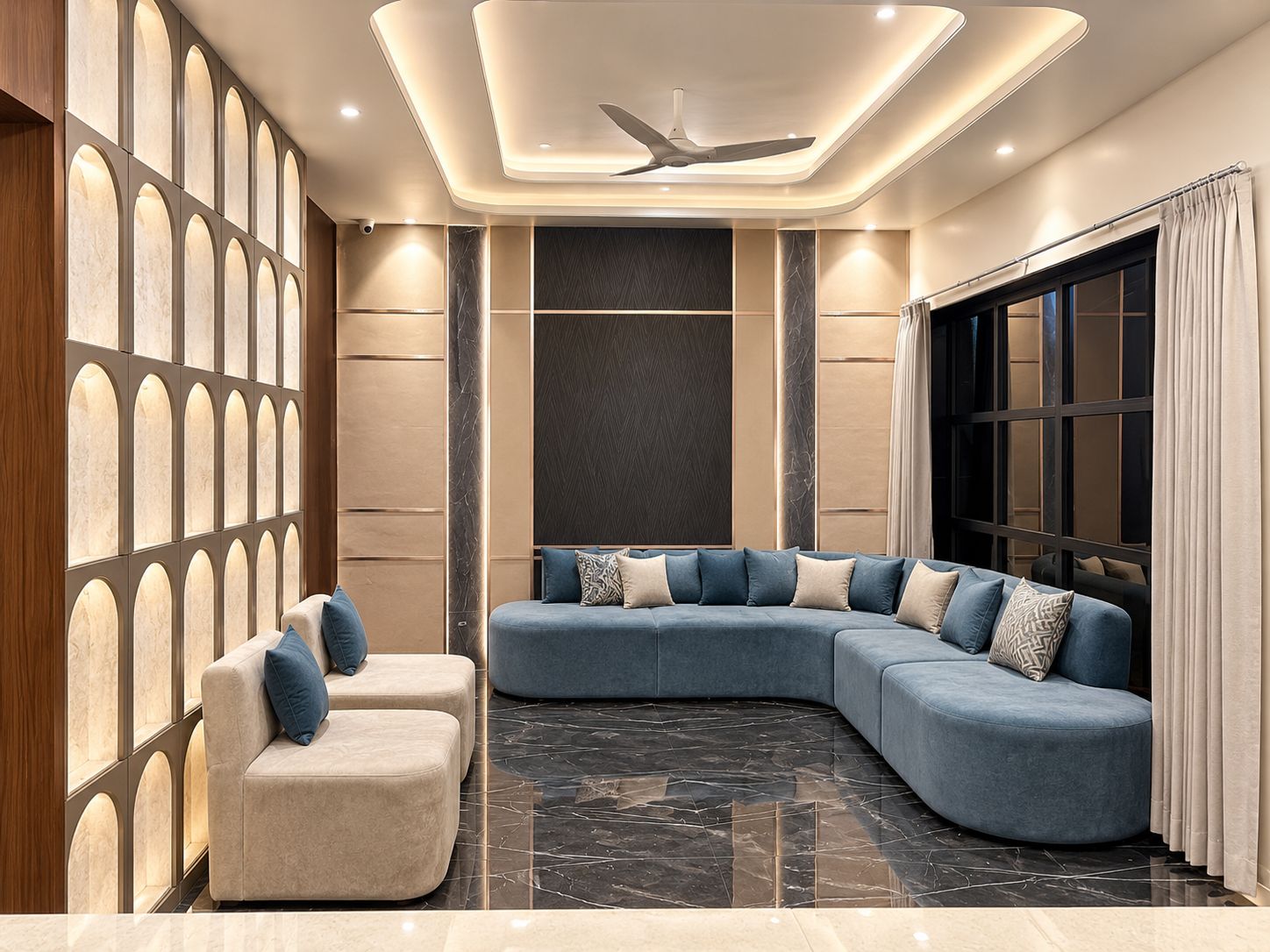 Una sala moderna con un sofá seccional curvo, un sillón beige pequeño y un ventilador de techo.