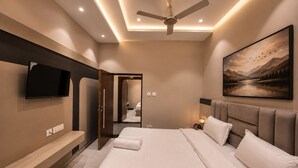 A modern hotel room with a large bed, a flat-screen TV mounted on the wall, a ceiling fan, and a painting of a landscape.