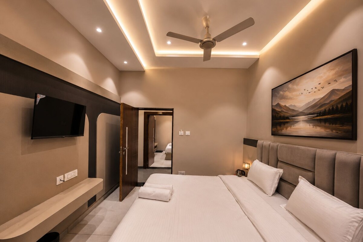 Una habitación de hotel moderna con una cama grande, un televisor de pantalla plana montado en la pared, un ventilador de techo y un cuadro de un paisaje.