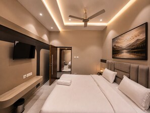 Una habitación de hotel moderna con una cama grande, un televisor de pantalla plana montado en la pared, un ventilador de techo y un cuadro de un paisaje.