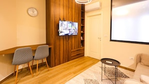 Une pièce avec un mur en bois, un téléviseur à écran plat fixé à ce mur, deux fauteuils gris, une petite table ronde et un canapé.