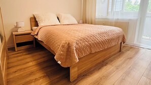 A bedroom with a wooden bed, a nightstand, a window with curtains, and two wall art pieces.