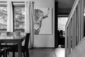 A dining area with a table and chairs, a painting on the wall, and a view of trees through the window. - Chalet Ember is a luxury mountain retreat near Breckenridge designed for large groups. Enjoy a private sauna, outdoor hot tub, fire pit, and warm modern alpine interiors—perfect for ski trips, multi-family getaways, and year-round mountain escapes. (Breckenridge)