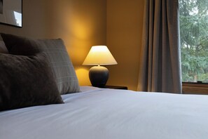 Hotellihuone, jossa on sänky, yöpöytä lampun kanssa ja ikkuna, jossa on verhot.