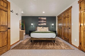 A bedroom with a bed, two bedside lamps, a nightstand, a mirror, and a large wooden wardrobe. - Chalet Ember is a luxury mountain retreat near Breckenridge designed for large groups. Enjoy a private sauna, outdoor hot tub, fire pit, and warm modern alpine interiors—perfect for ski trips, multi-family getaways, and year-round mountain escapes. (Breckenridge)