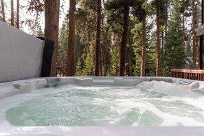 A hot tub surrounded by tall trees, with a wooden deck in the background. - Chalet Ember is a luxury mountain retreat near Breckenridge designed for large groups. Enjoy a private sauna, outdoor hot tub, fire pit, and warm modern alpine interiors—perfect for ski trips, multi-family getaways, and year-round mountain escapes. (Breckenridge)