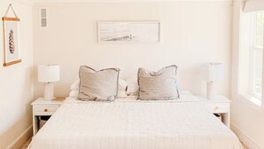 Une chambre avec un grand lit, deux tables de chevet avec des lampes, un ventilateur de plafond et un tableau encadré au mur.