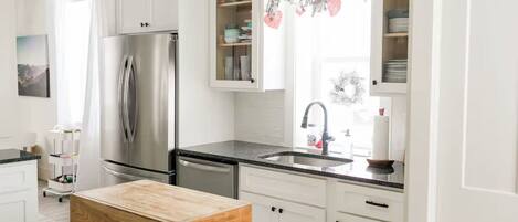 A modern kitchen with white cabinetry, a stainless steel refrigerator, a wooden island, and a window with holiday decorations.