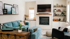 Un salon avec un canapé bleu, une table basse, une chemin ée, un téléviseur et une bibliothèque.