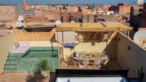 A rooftop terrace with a pool, dining area, and a view of the cityscape. - Riad KAMA privatif (Marrakech)