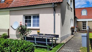 A building with a satellite dish, a window with a white frame, a door, and a small garden area with a bench and flowers. - Quietly located vacation apartment in idyllic surroundings - relaxation guaranteed (Groß Lindow)
