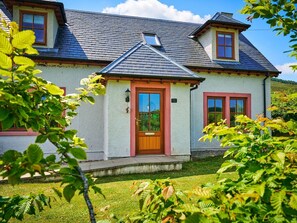 Une maison à deux étages avec un toit en pente, une entrée à l’avant avec une porte en bois et un petit porche.