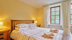 Ein ordentlich bezogenes Bett mit einer Karo-Bettdecke, zwei Nachttischlampen und einem Fenster mit Vorhängen.