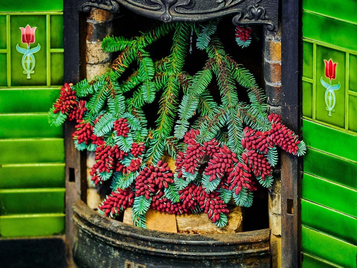 A fireplace with green walls and a decorative pine branch with red cones.