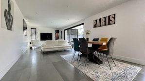 Una sala de estar moderna con un sofá blanco, una mesa de comedor con sillas y un ventanal grande.